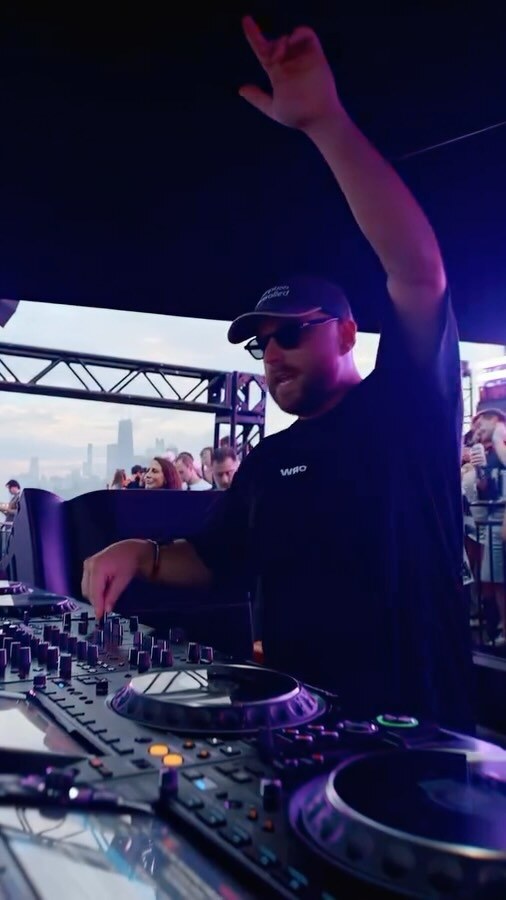 Biscits performs behind a DJ deck with one arm raised.