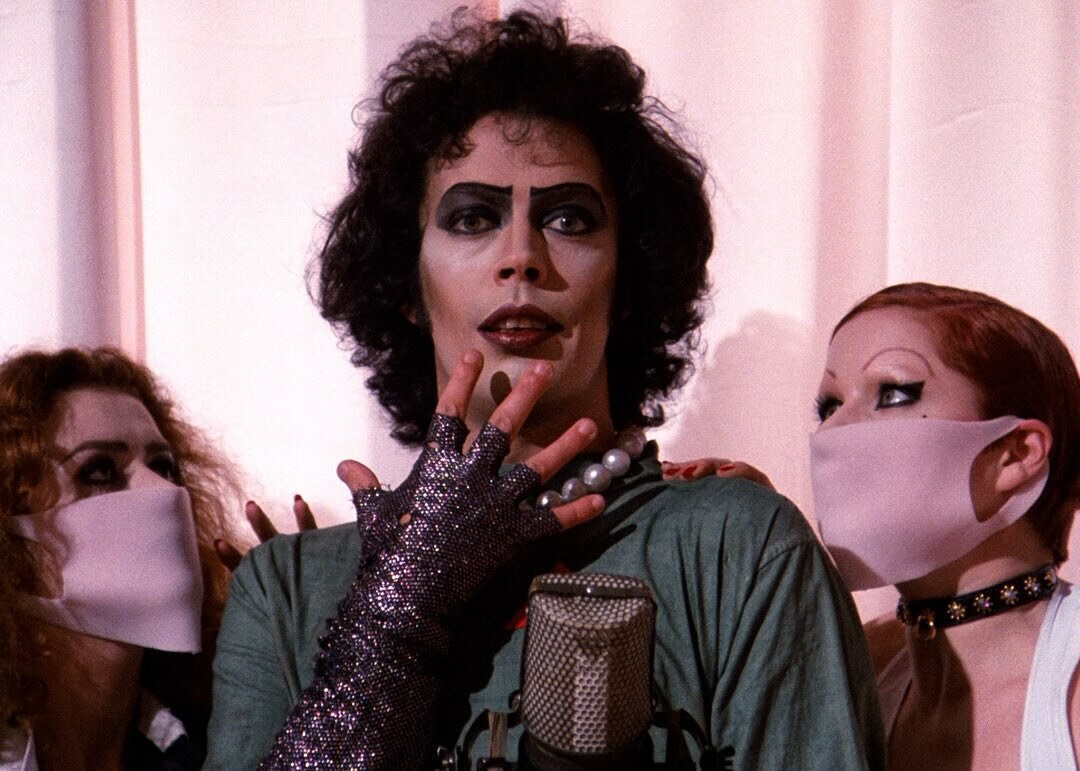 Tim Curry as Dr. Frank-N-Furter poses between two masked attendants in The Rocky Horror Picture Show.
