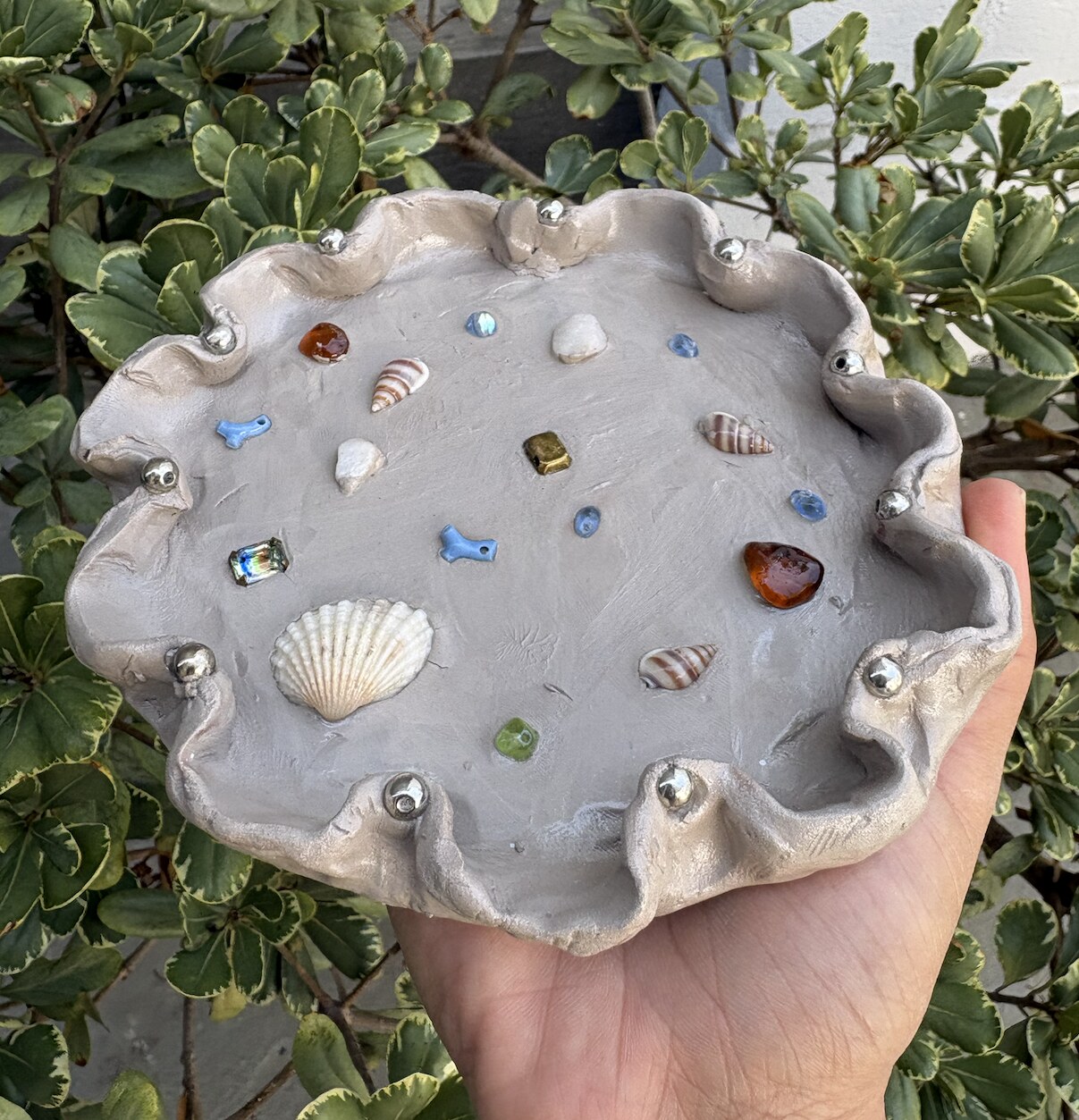 Handmade scalloped clay trinket dish decorated with shells and beads.