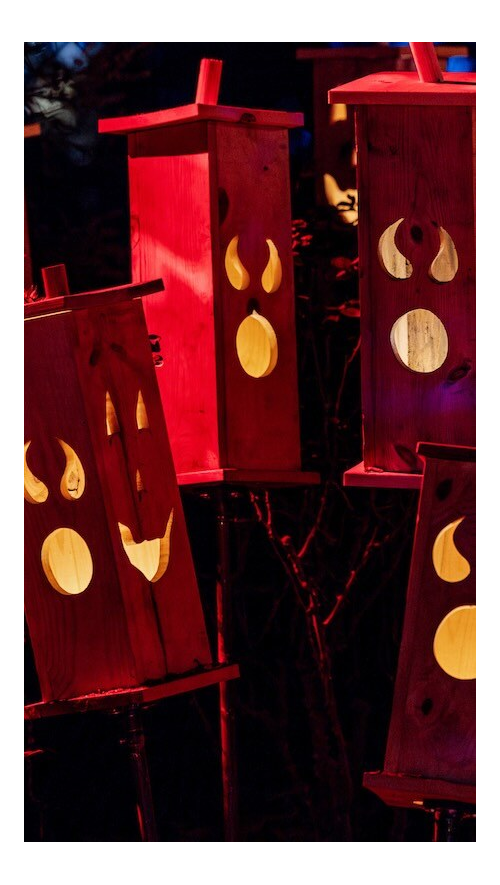 Red-lit wooden spirit lanterns glowing among the nighttime gardens for Descanso Gardens' Carved celebration.