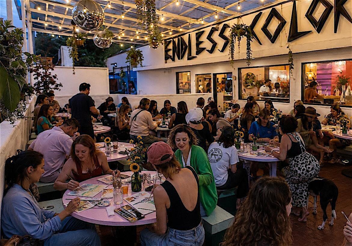 People painting with watercolors at colorful communal tables at Endless Color.