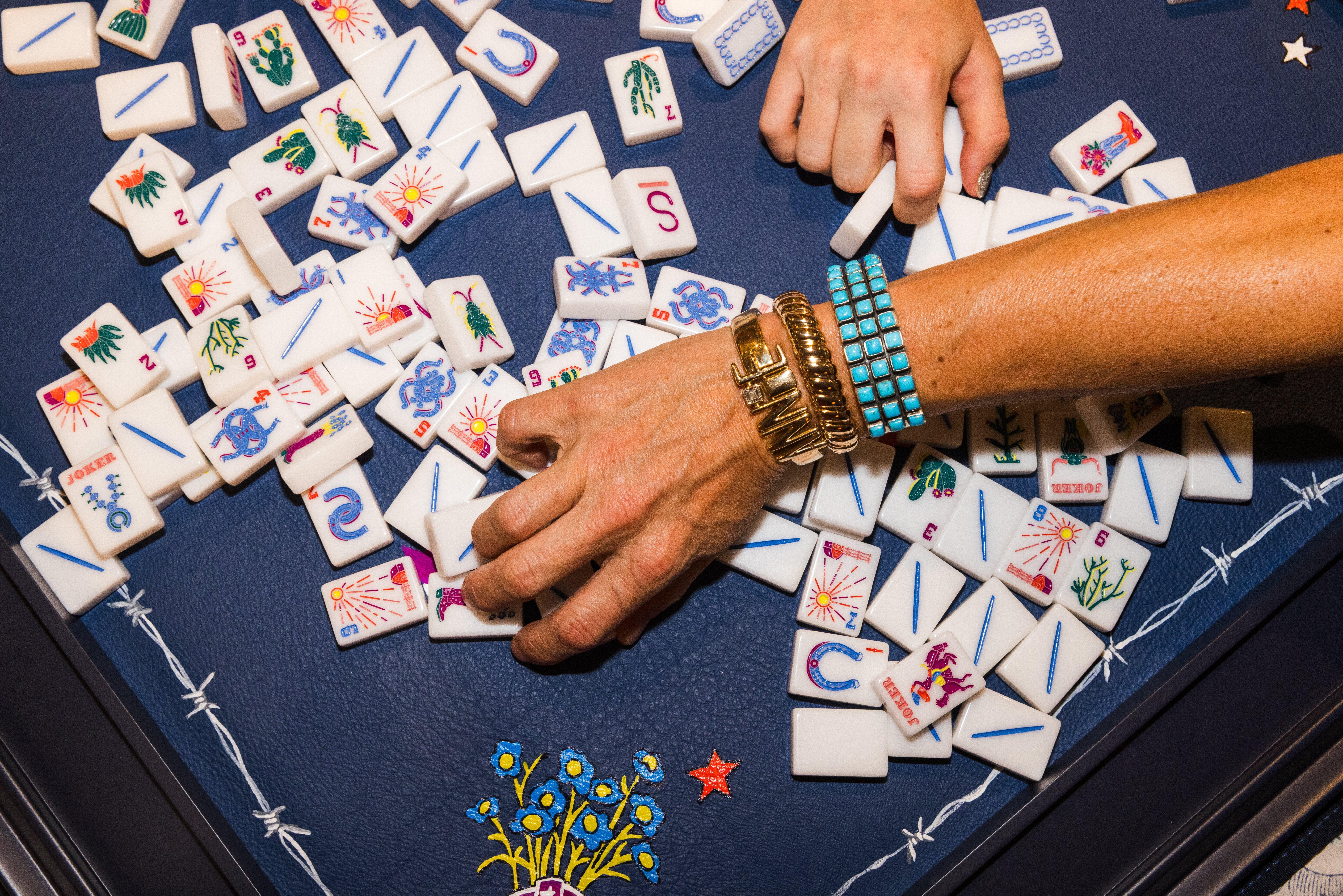 Hands mixing colorful American mahjong tiles on a blue playing mat.