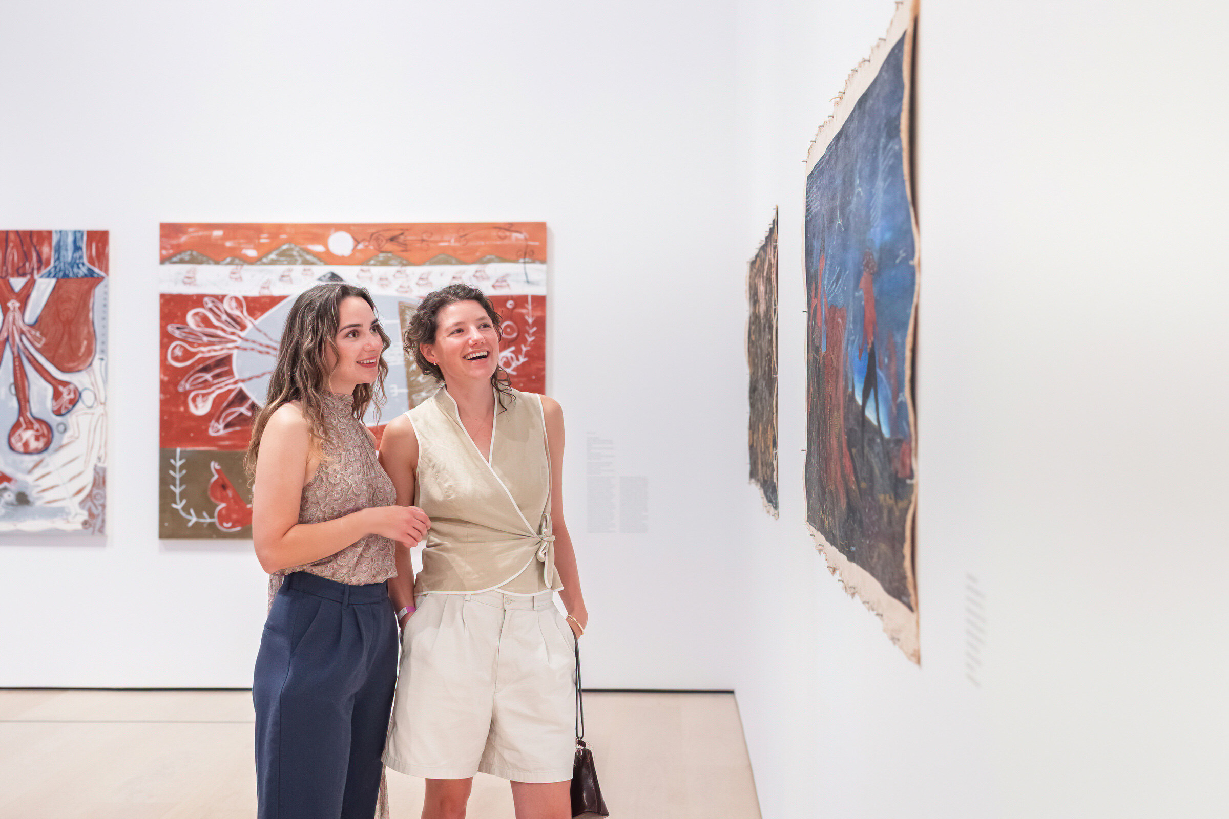 Two women look at a painting on a gallery wall together